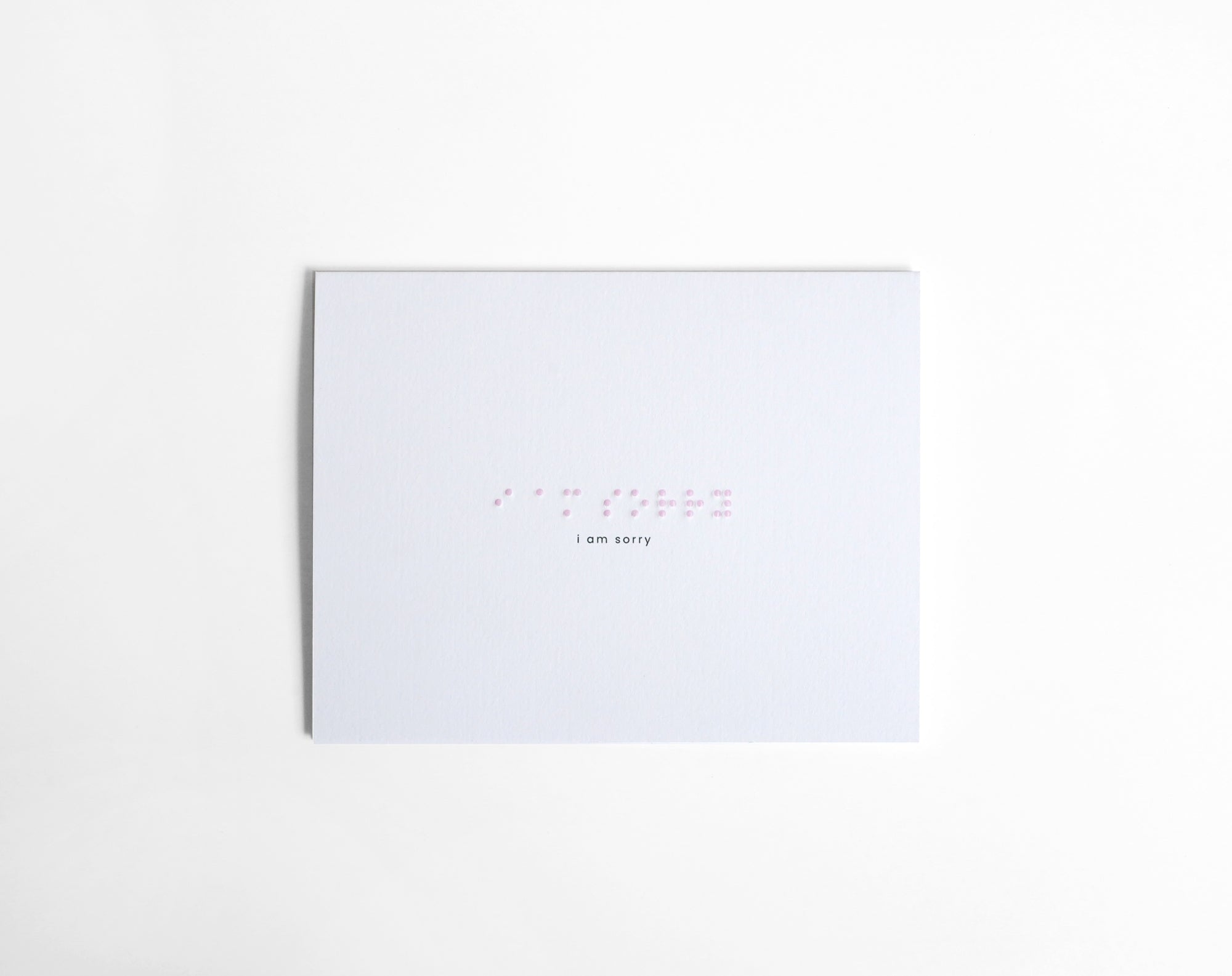 White greeting card with “I Am Sorry” embossed in soft pink Braille, paired with a white envelope. Elegant, handmade card crafted with precision and care.