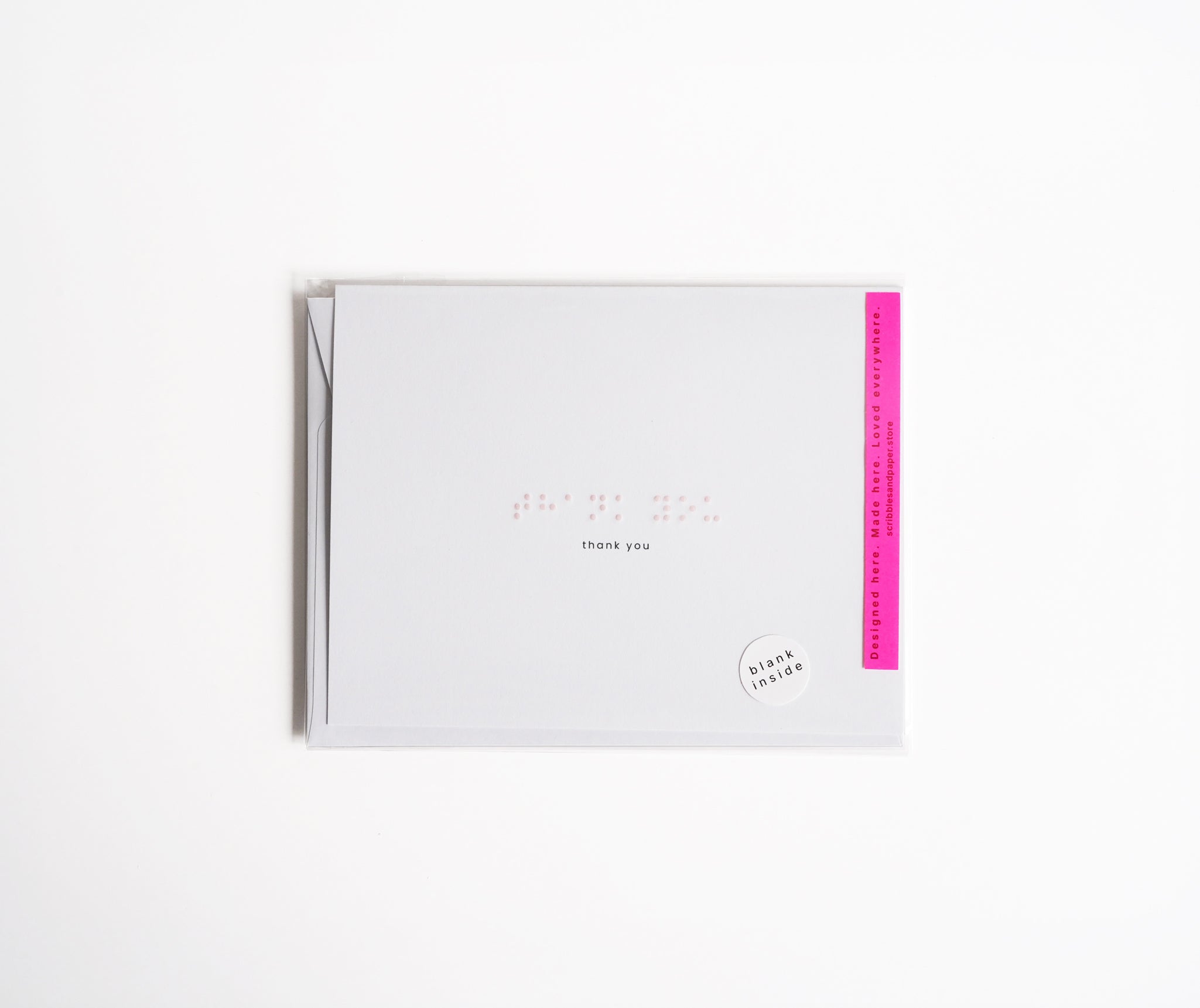 White greeting card with “Thank You” embossed in light pink Braille.