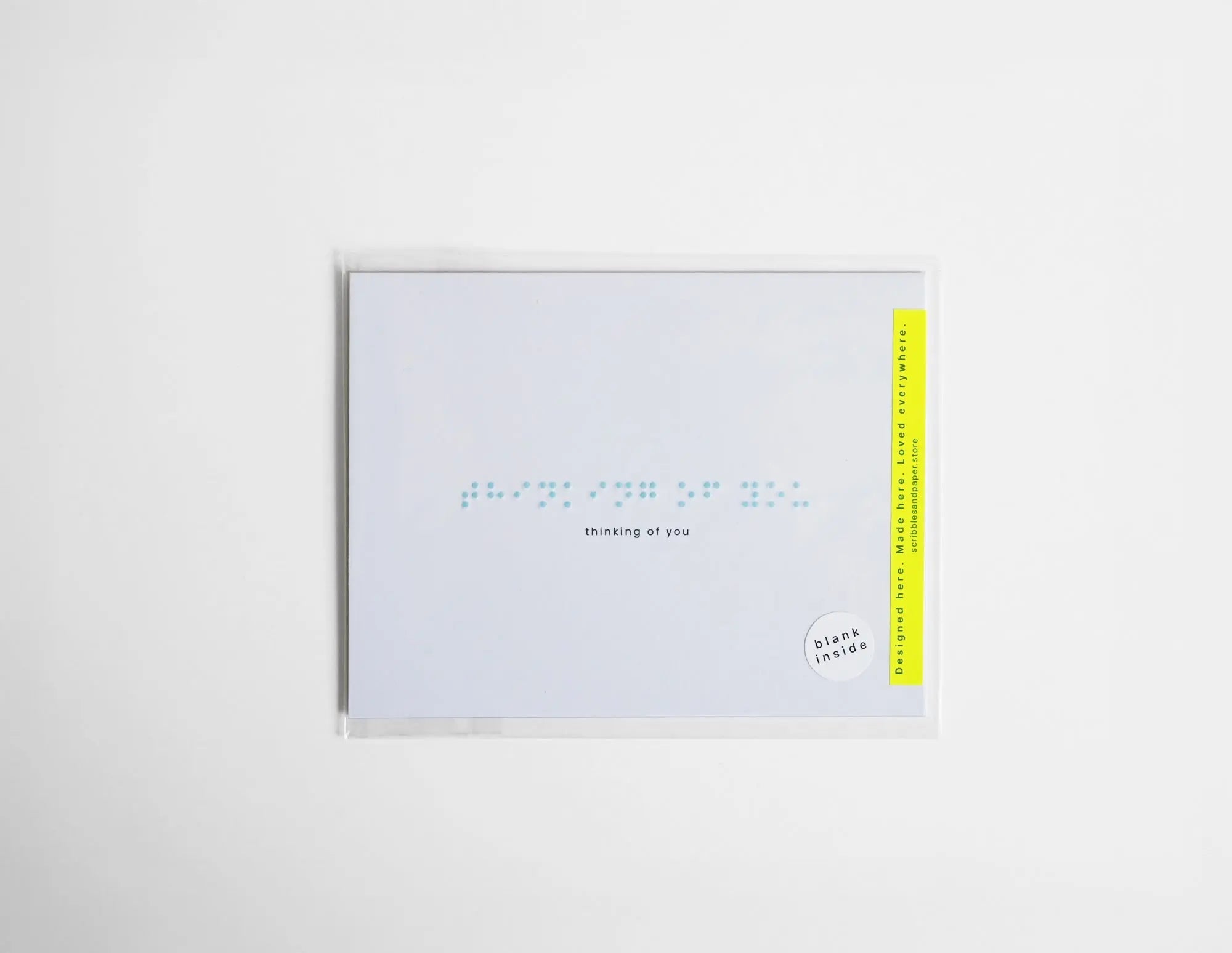 White greeting card with “Thinking of You” embossed in light blue Braille.