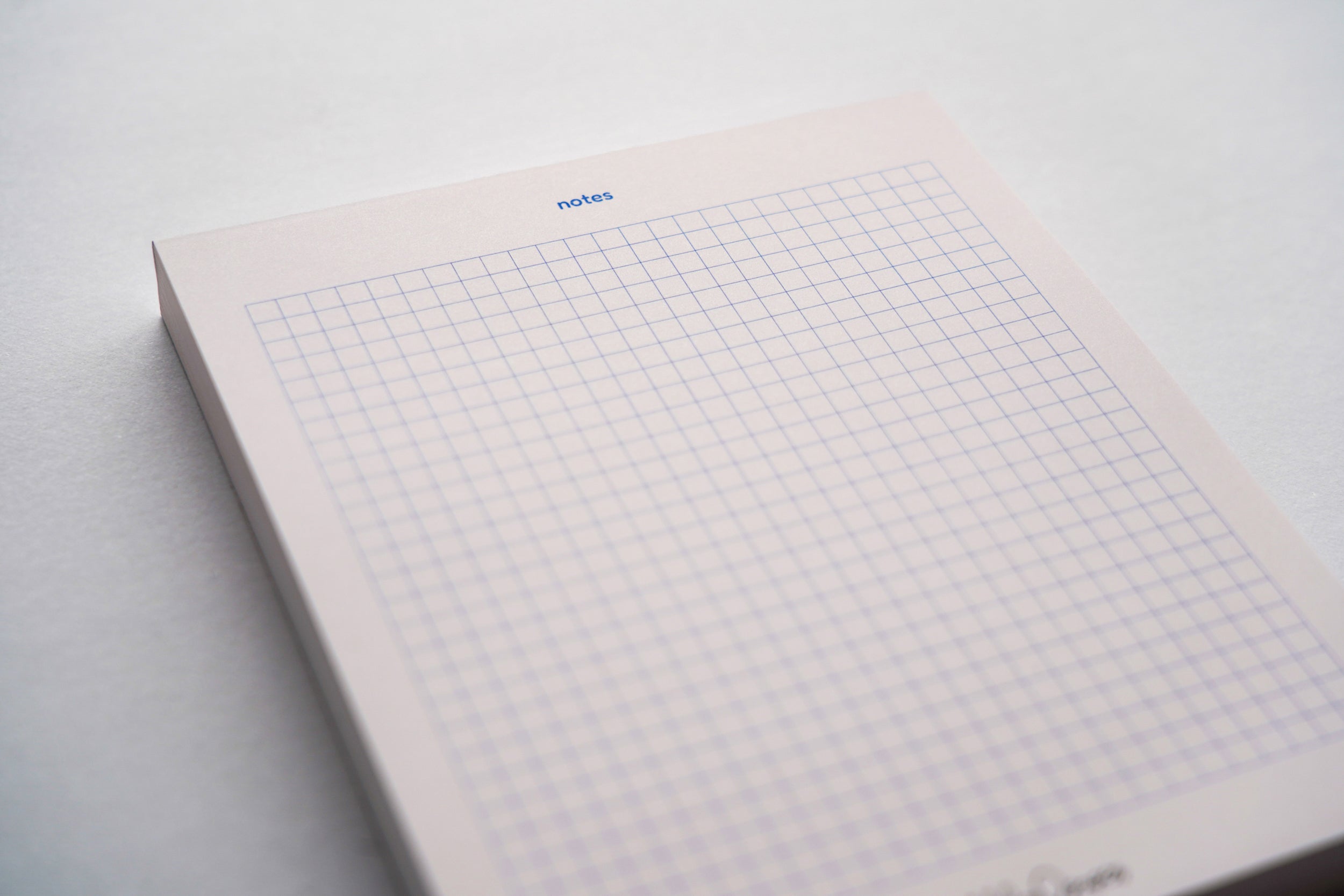 Modern pink notepad with graphic blue grid and notes heading – 100-page stationery. (front view)